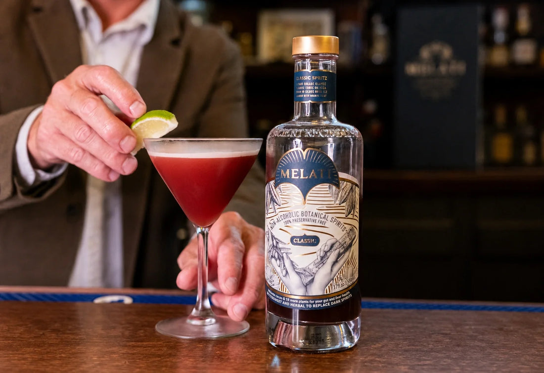 Bartender garnishing a red cocktail beside a Melati Drinks Classic bottle on a wooden bar.