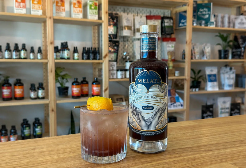 Melati Drinks Classic bottle beside a citrus-garnished botanical spritz on a wooden counter.