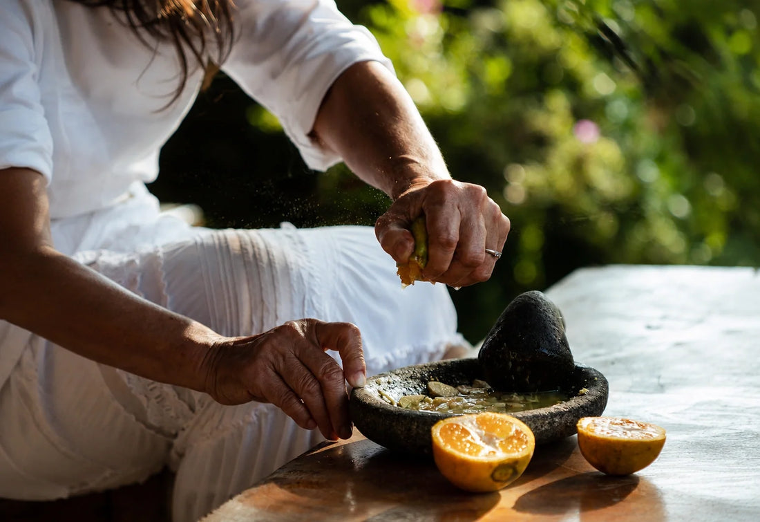 A woman squeezes fresh citrus into a stone mortar while preparing botanicals for Melati.